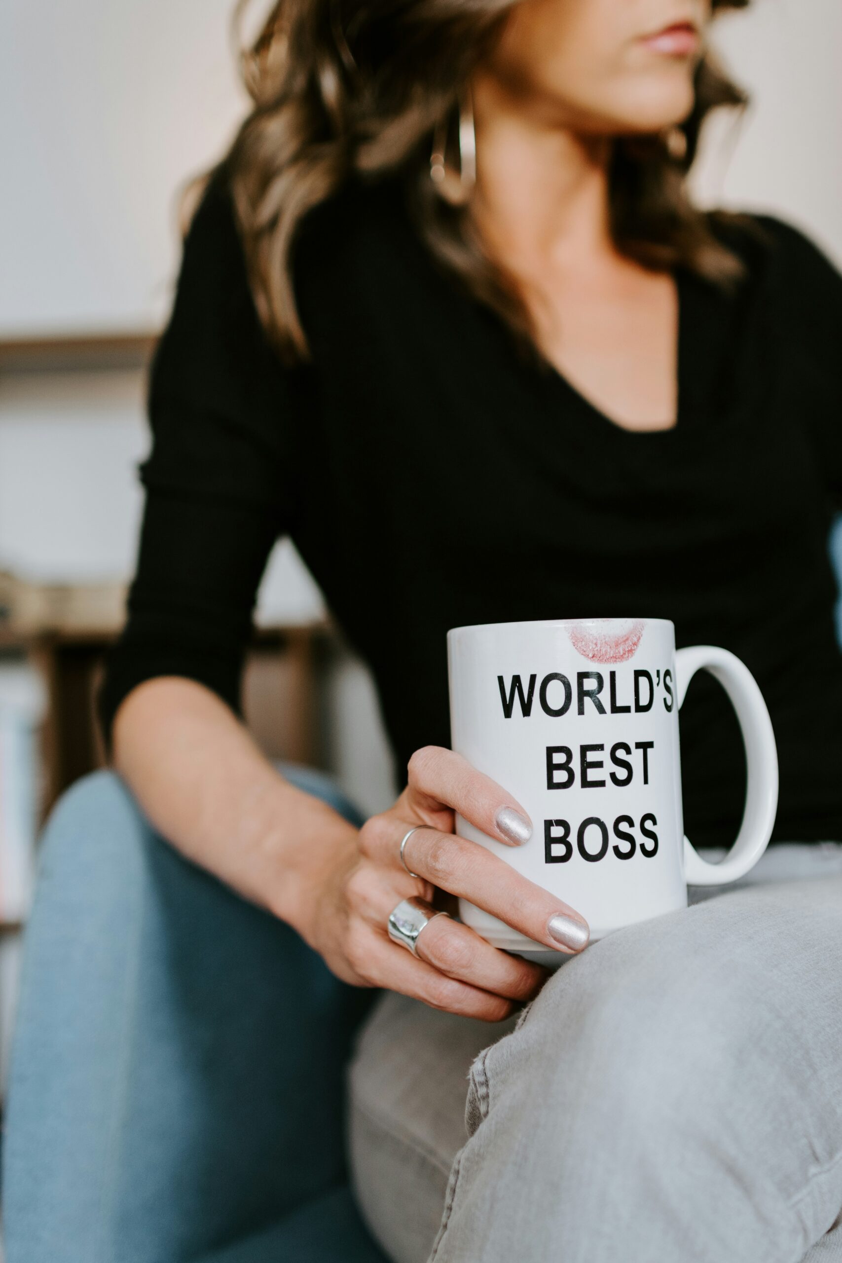 Professional woman looking away from camera, holding a coffee mug that reads, "World's best boss" with a lipstick stain.